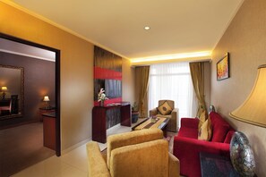 A hotel room with a desk, two chairs, a sofa, a TV, and a large mirror. - Lion Hotel & Plaza (Manado)