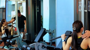 A gym with exercise equipment, a mirror, and a person assisting another person.