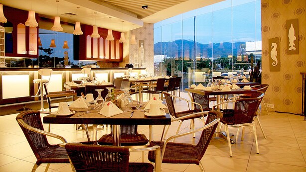 A modern restaurant with high ceilings, pendant lighting, and a view of mountains through large windows.