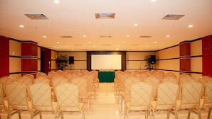 A conference room with rows of chairs, a projector screen, and a speaker.
