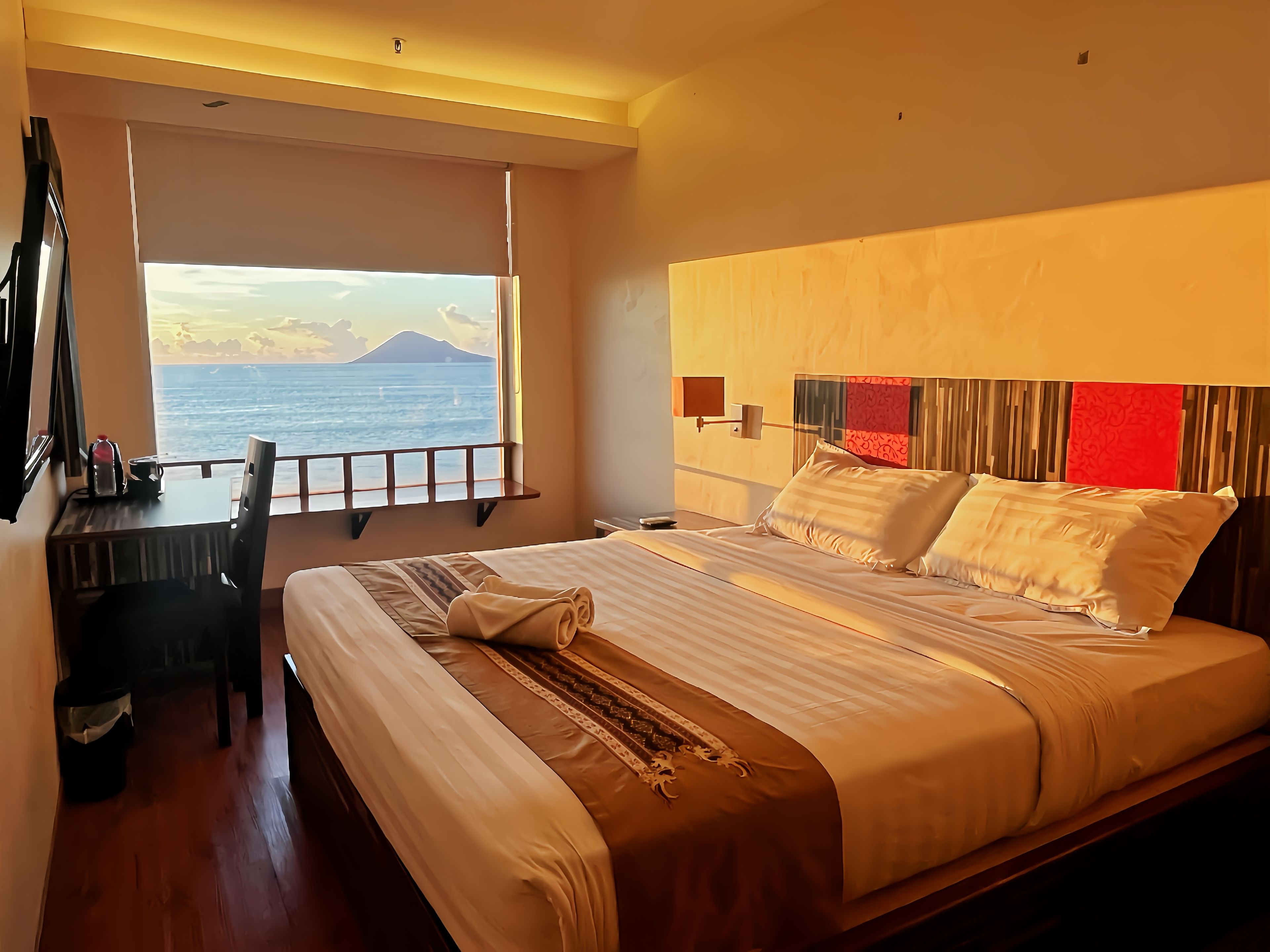 A hotel room with a bed, a desk, and a view of the sea.