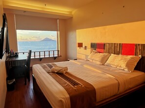 A hotel room with a bed, a desk, and a view of the sea. - Lion Hotel & Plaza (Manado)