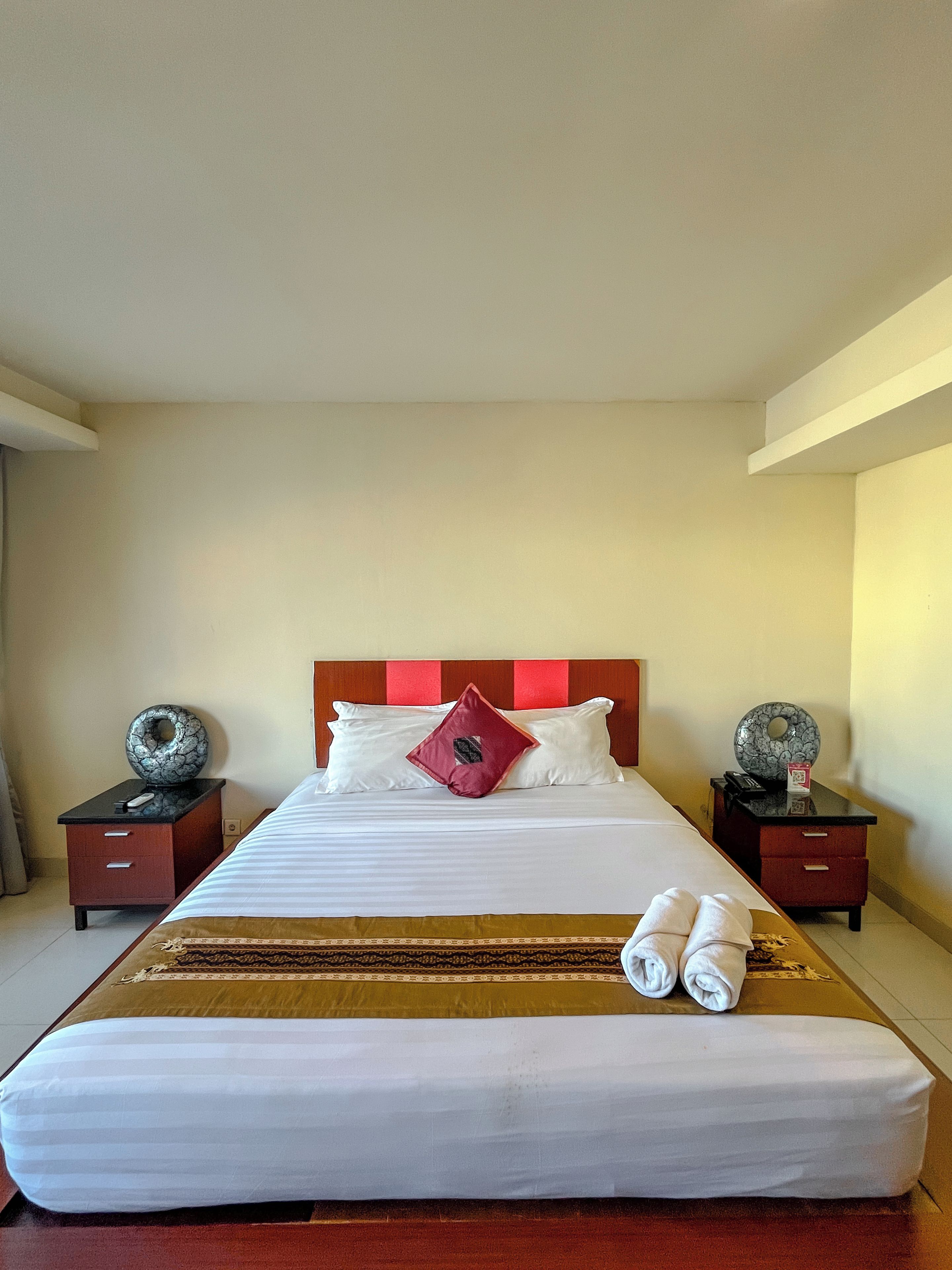 A hotel room with a large bed, two bedside tables, and a headboard with a red accent.