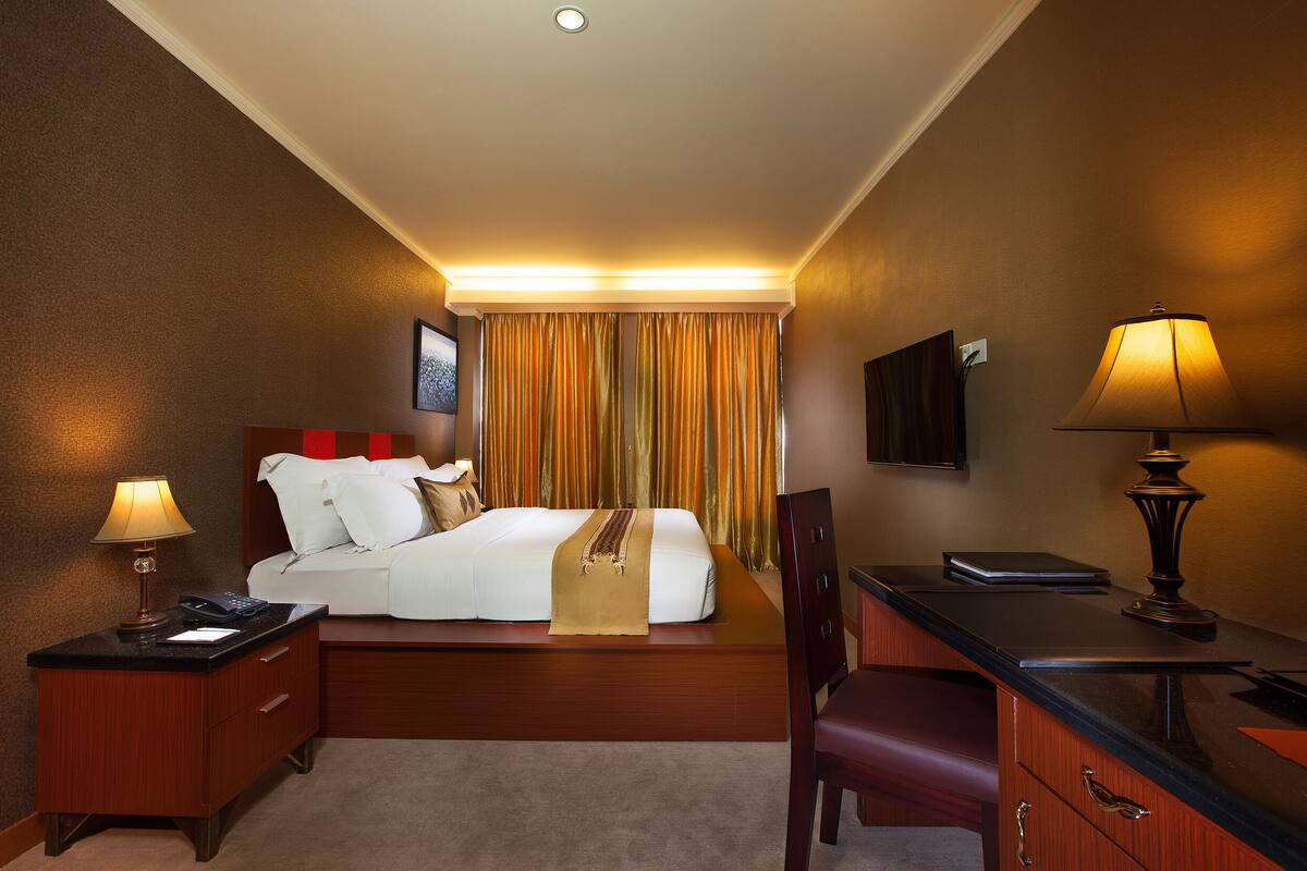 A hotel room with a bed, bedside table, desk, chair, and a TV on the wall.