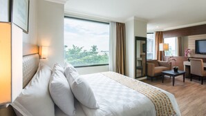 A hotel room with a large bed, a desk, a chair, a television, and a view of the outdoors. - Almadera Hotel Makassar (Makassar)