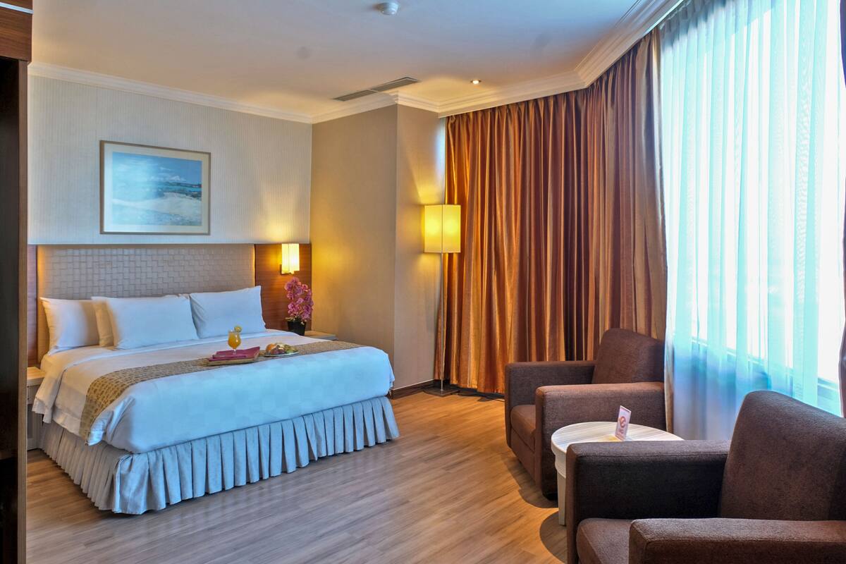 A hotel room with a large bed, two armchairs, a small table, a lamp, and a painting on the wall.