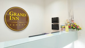 Un espace d’accueil avec une enseigne indiquant « Grand Inn », un comptoir en verre et une composition florale.