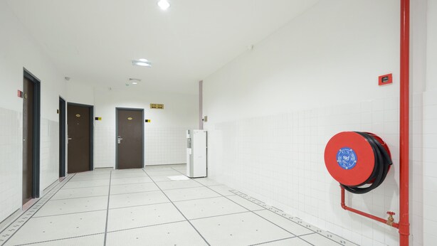 A hallway with white tiled floors, doors, and a red fire hose reel. - Grand Inn Penang Road (George Town)