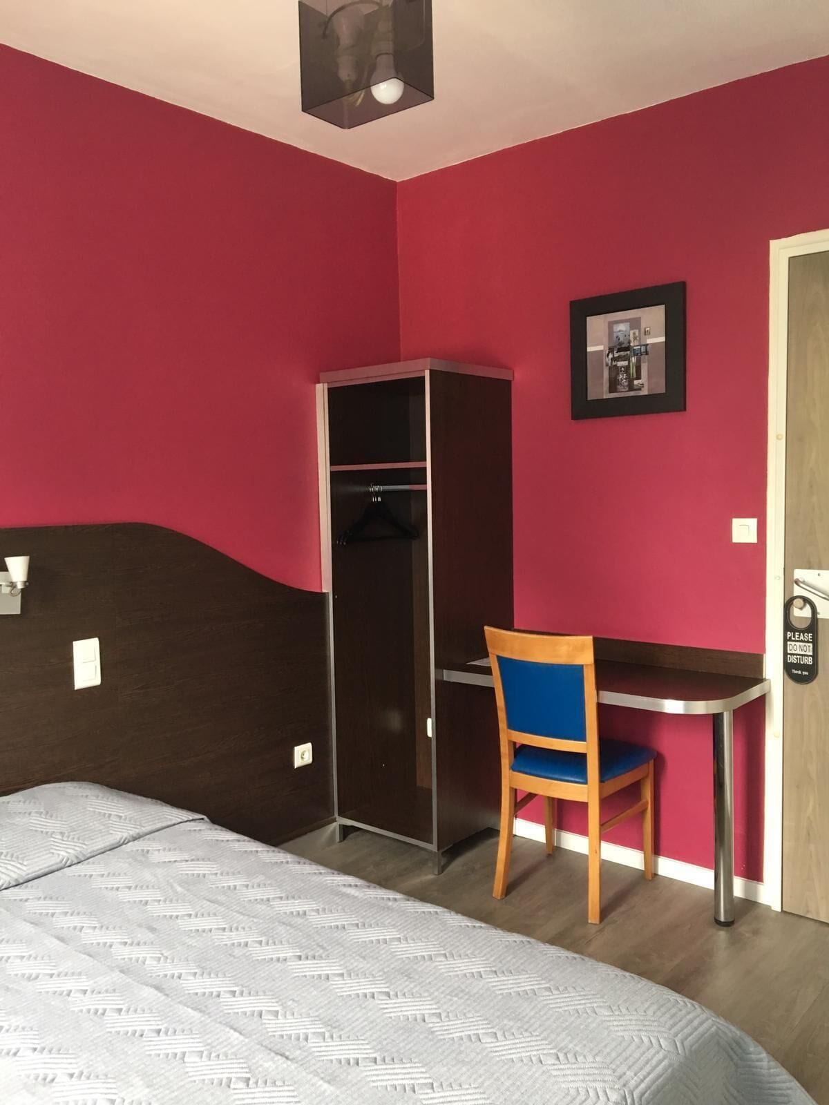 Un dormitorio con cama, escritorio, silla, armario y una puerta con el letrero 'No molestar'.