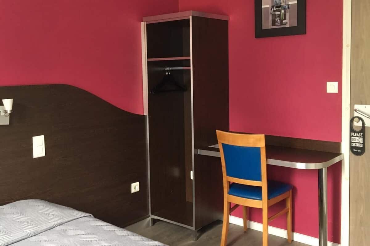 A bedroom with a bed, a desk, a chair, a wardrobe, and a door with a 'Please do not disturb' sign.
