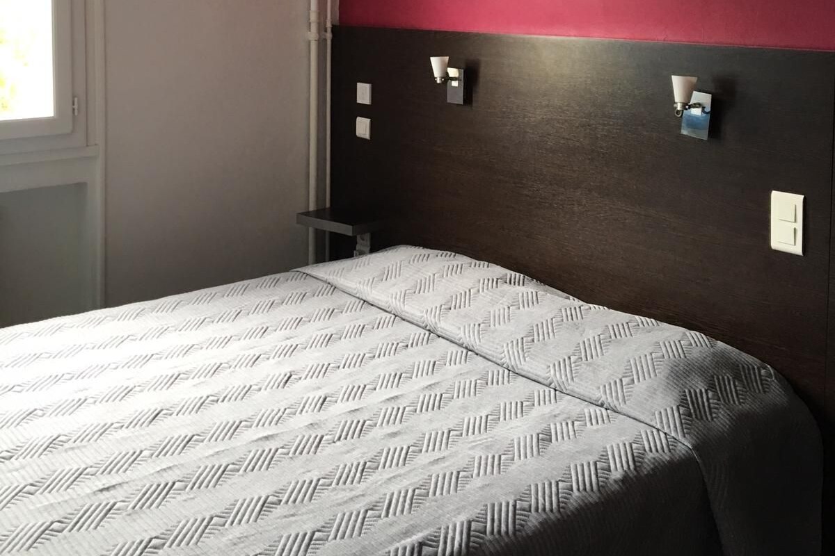A bedroom with a bed, a window, and a wall with two wall-mounted light fixtures.
