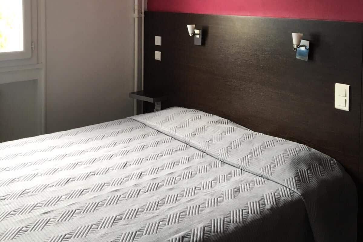 A bedroom with a bed, a window, and a wall with two wall-mounted light fixtures.
