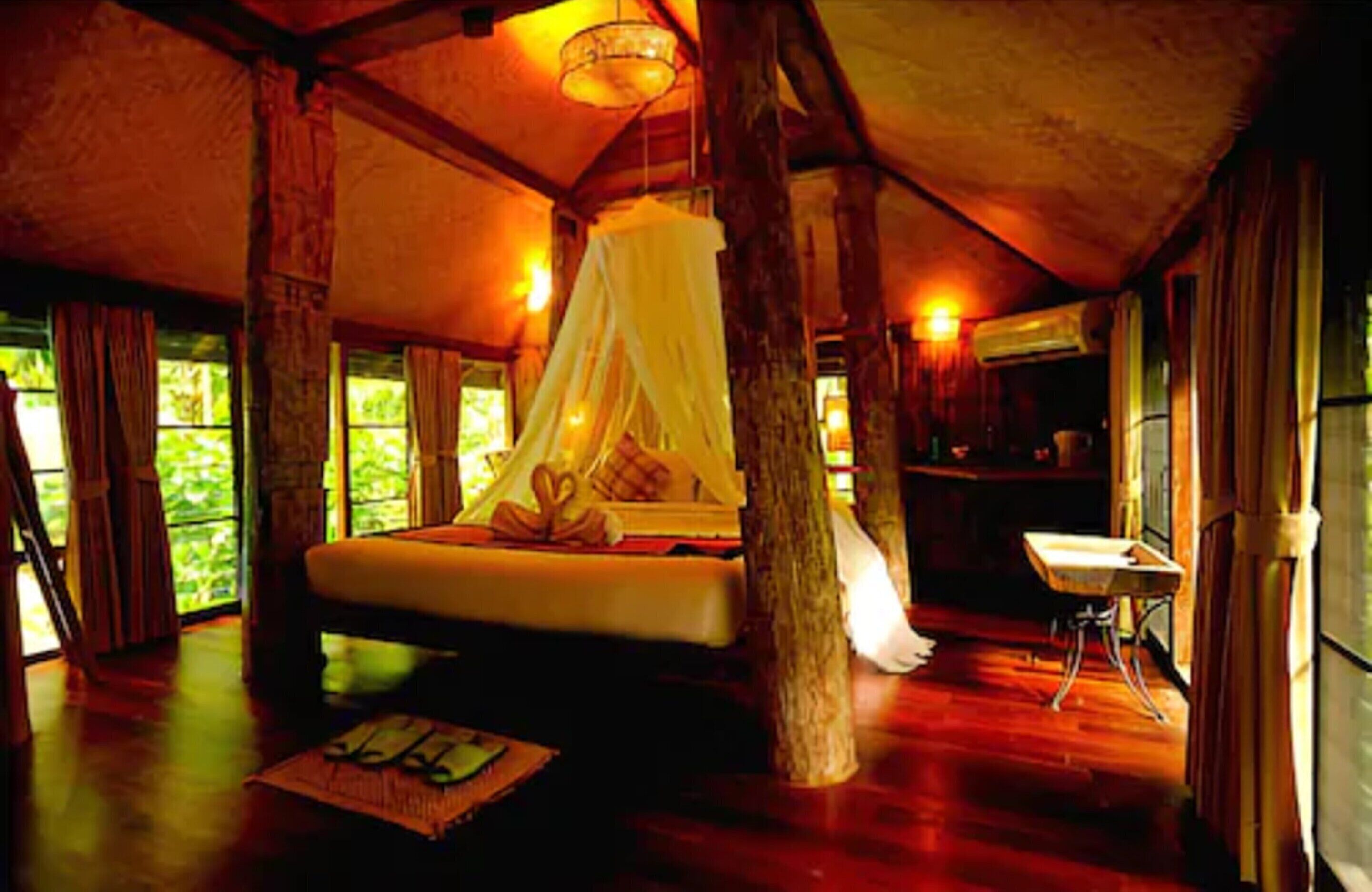 A cozy bedroom with a canopy bed, wooden beams, and large windows.