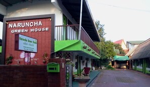 The exterior of Naruncha Green House, featuring a prominent green facade, a visible entrance, and a small outdoor seating area.