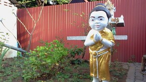 A statue of a person in traditional attire standing in front of a red fence. - Naruncha Green House (Chiang Mai)