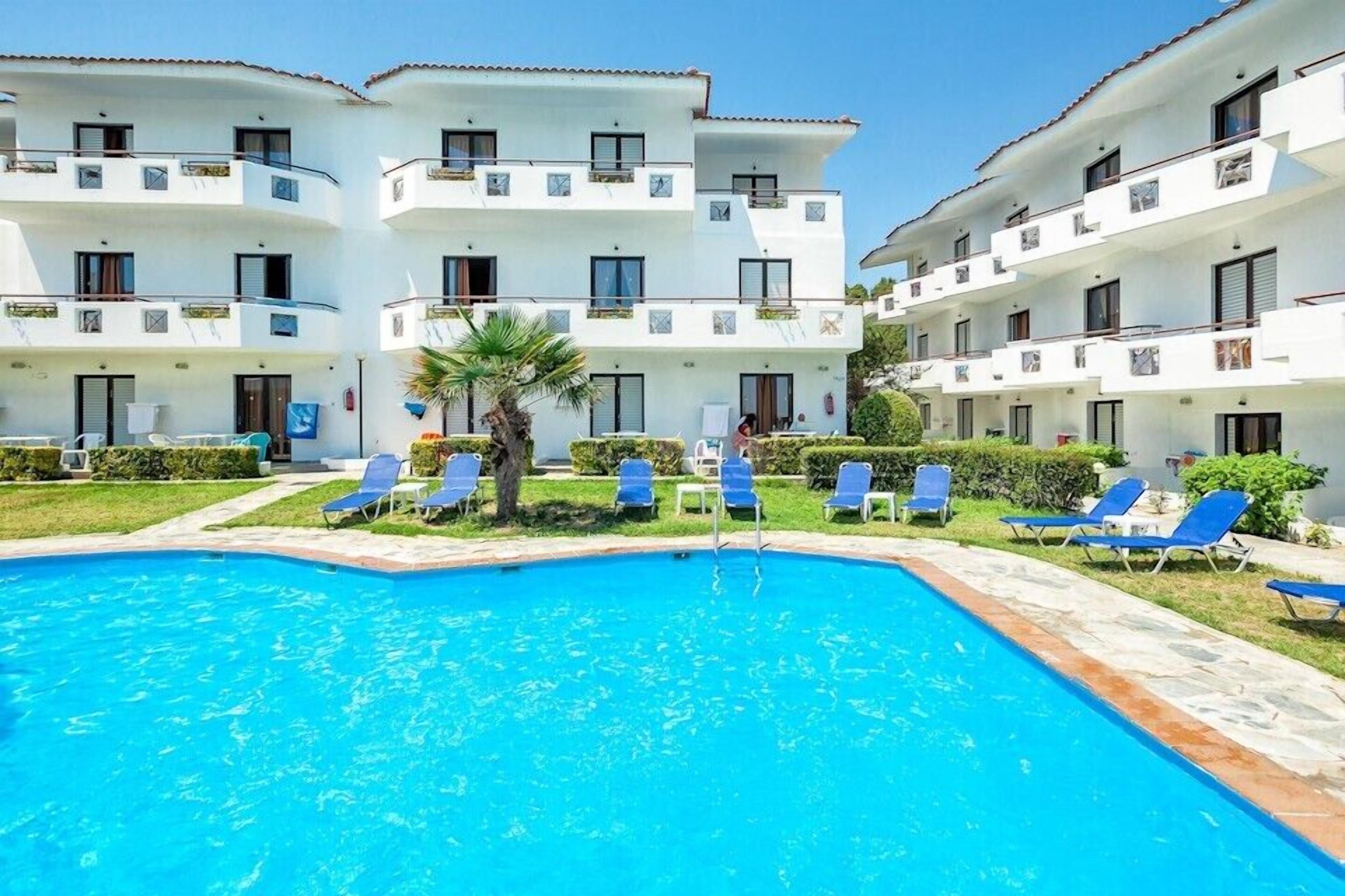 A hotel with a swimming pool surrounded by blue lounge chairs.