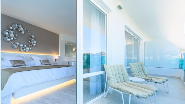 A modern bedroom with a large bed, a decorative wall piece, and a balcony with two lounge chairs. - Plaza Santa Ponsa Boutique Hotel - Adults Only (Calvia)