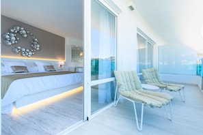 Une chambre moderne avec un grand lit, un élément décoratif mural et un balcon agrémenté de deux fauteuils de relaxation.