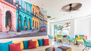 A modern hotel lobby with colorful seating, a large mural of a street scene, and a view of the city. - Plaza Santa Ponsa Boutique Hotel - Adults Only (Calvia)