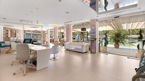 A spacious hotel lobby with a modern design, featuring a white reception desk, comfortable seating areas, and large windows offering views of the outdoors. - Plaza Santa Ponsa Boutique Hotel - Adults Only (Calvia)