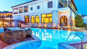 Un hotel de dos pisos con piscina, sillas de descanso y fachada de piedra.
