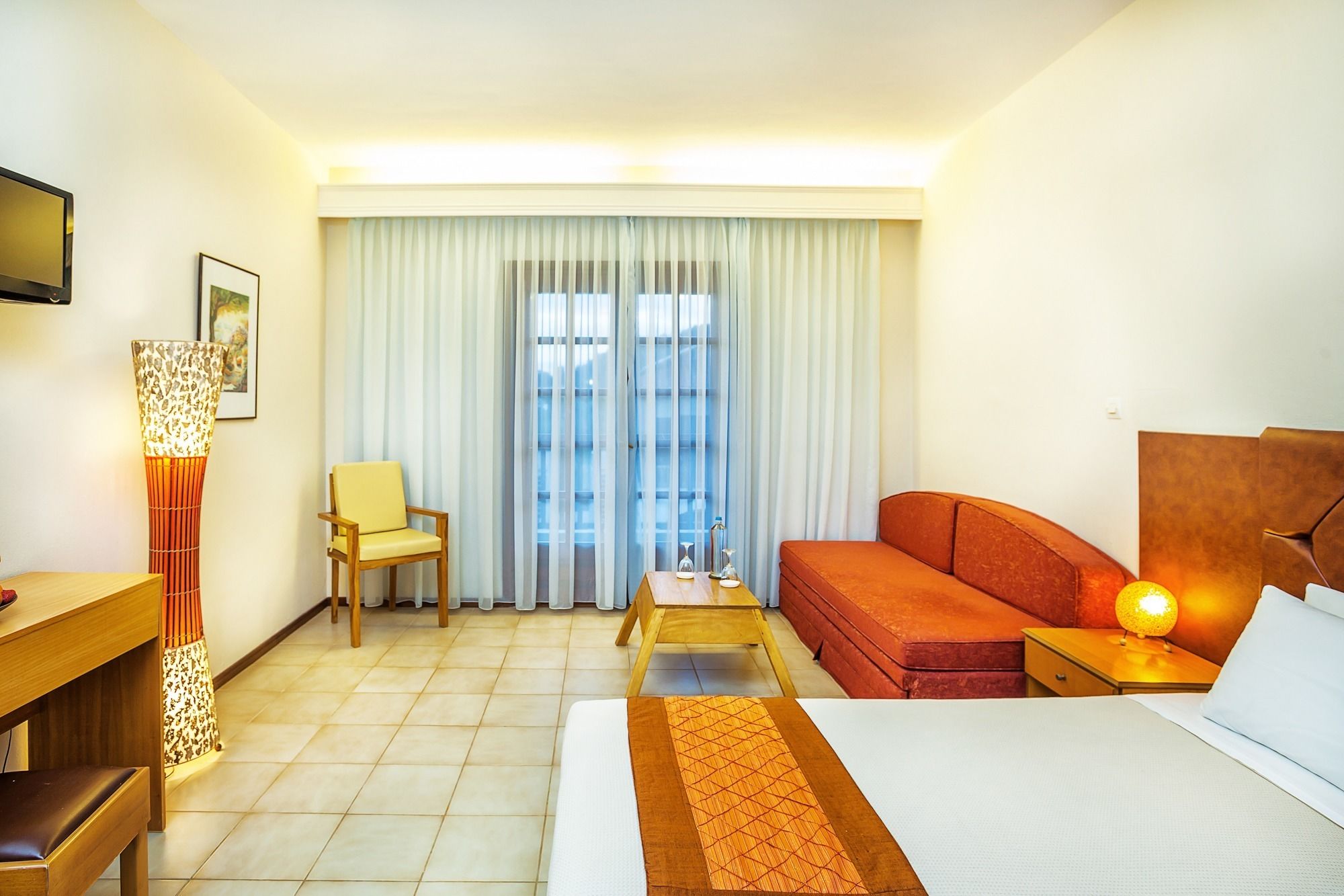 A hotel room with a bed, a sofa, a chair, a desk, and a lamp.