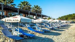 Una playa con filas de sillones reclinables azul y blanco y sombrillas blancas, identificada con el rótulo 'El Ron de Cuba'.