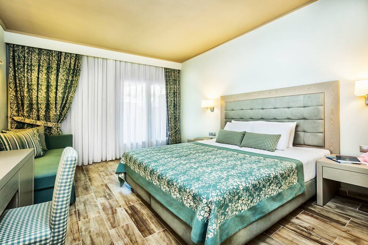 A hotel room with a large bed, a desk, a chair, and a window with curtains.