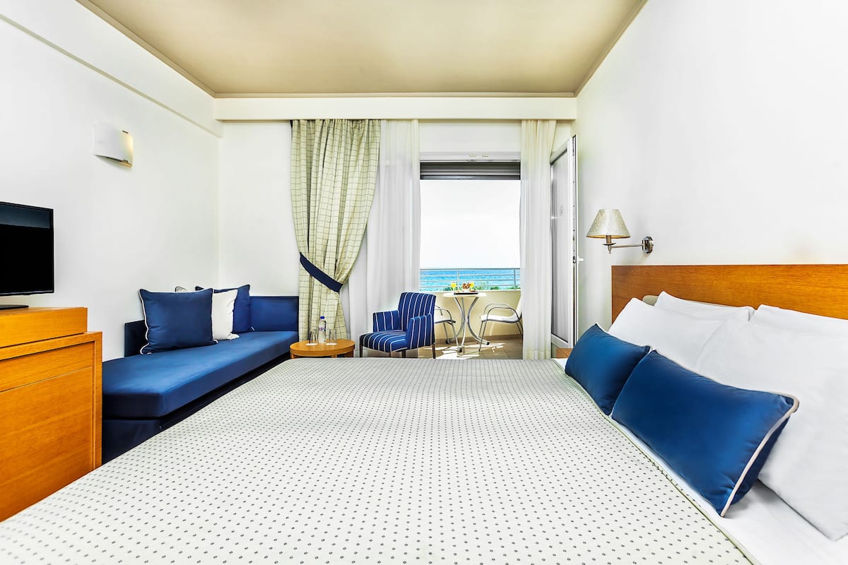 A hotel room with a bed, a sofa, a TV, a desk, and a view of the sea.
