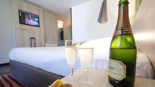 A hotel room with a bed, two glasses of champagne, a bottle of champagne, and two macarons on a small table.