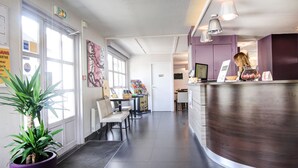 A reception area with a reception desk, chairs, a potted plant, and a large window.