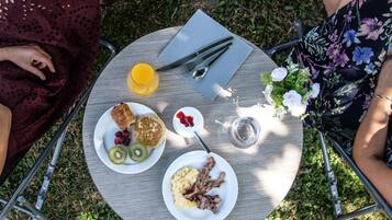 A round metal table with a white plate containing pancakes, kiwi, raspberries, and a glass of orange juice.
