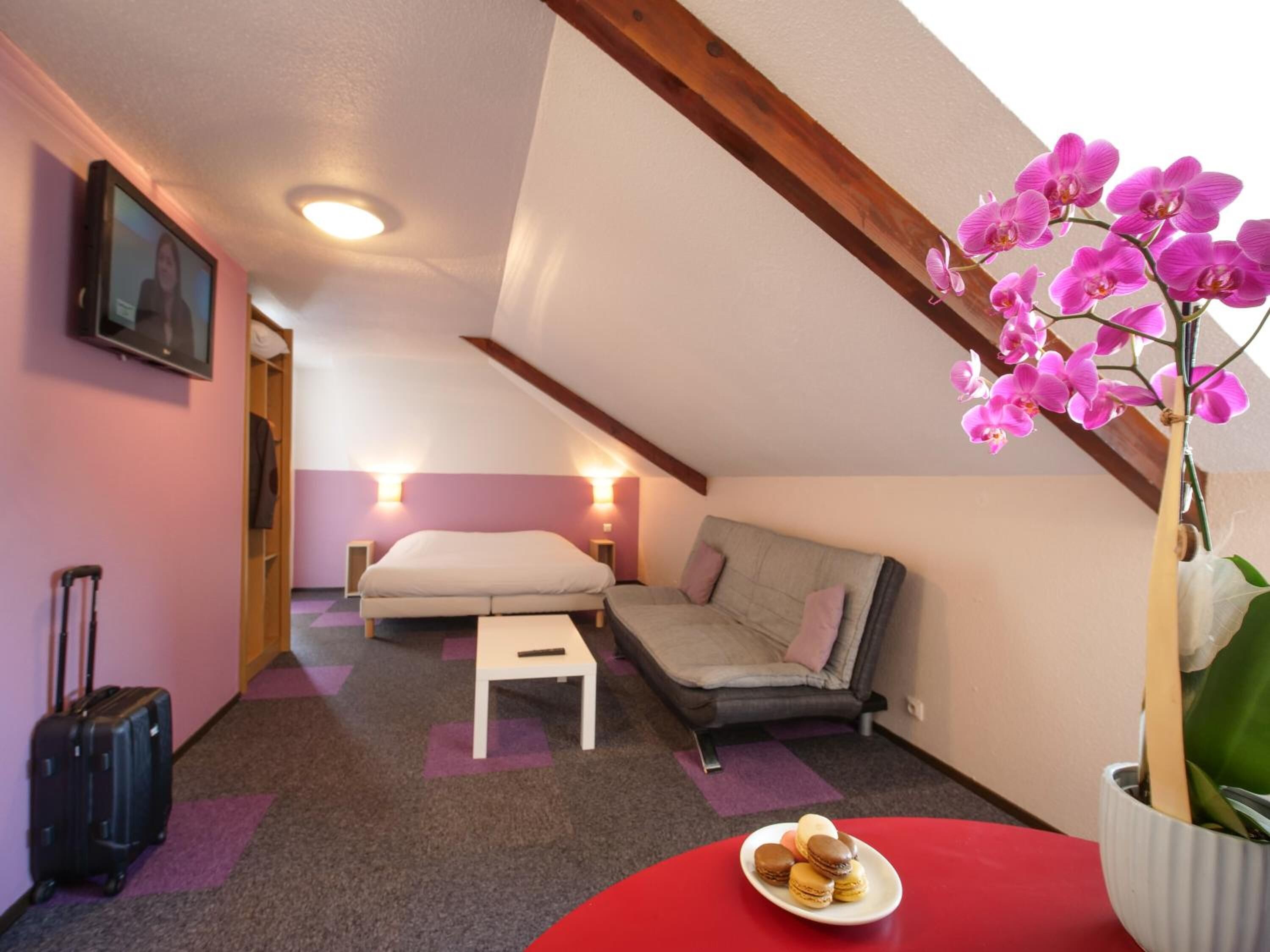 A cozy room with a bed, a sofa, a small table, and a red table with macarons.