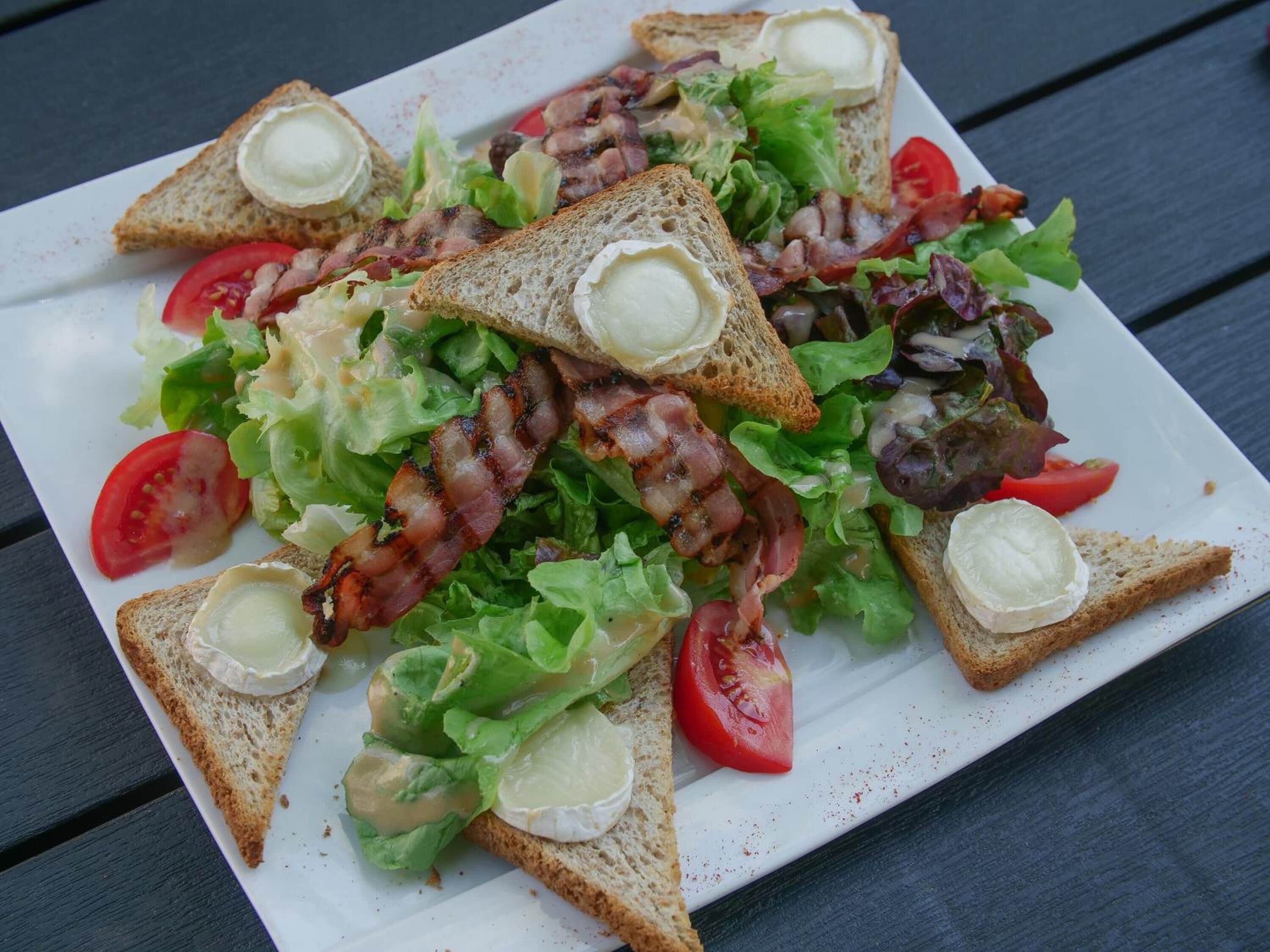 A plate of food consisting of toasted bread, bacon, lettuce, tomatoes, and cheese.