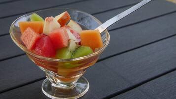 En glasskål med blandad frukt står på en träyta.
