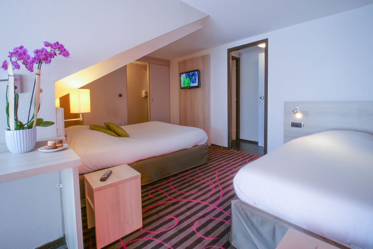 Une chambre d’hôtel avec un lit, un bureau doté d’une lampe, une télévision et une orchidée en pot.