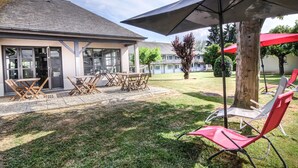 An outdoor patio area with a table and chairs, a large umbrella, and red lounge chairs.