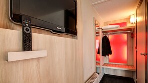 A modern hotel room with a mounted TV, a white shelf, a red-lit window seat, and a radiator.