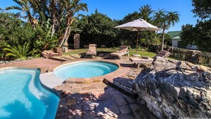 A swimming pool with a stone border, surrounded by lounge chairs and an umbrella. - Dune Ridge Country House (Saint Francis Bay)