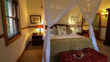 A bedroom with a four-poster bed, a nightstand with a lamp, and a red ottoman with a tray of wine glasses.