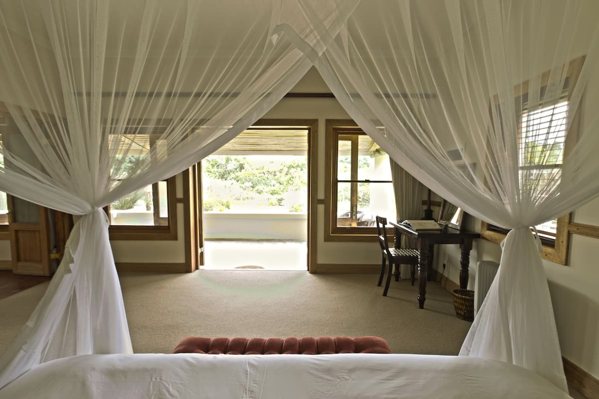 A bedroom with a bed, a desk, and a chair. There are windows with curtains.