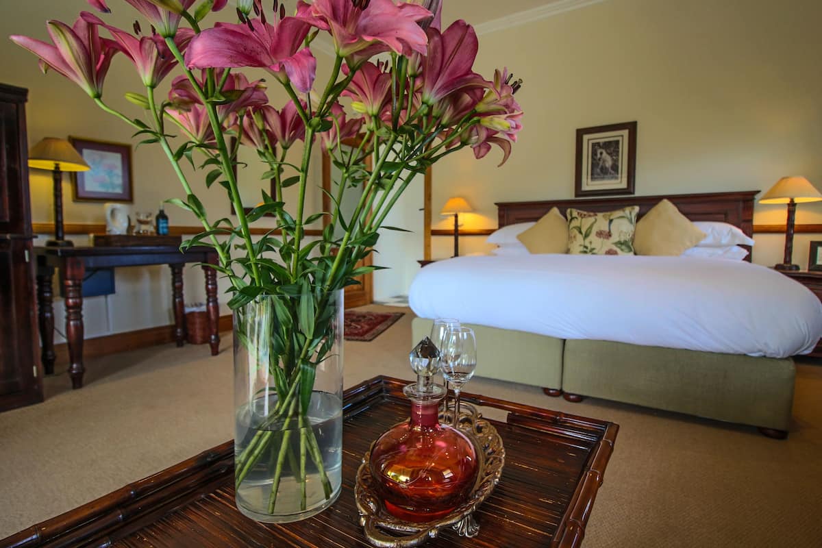 A hotel room with a bed, bedside lamps, a vase with flowers, and a tray with a bottle and glasses.