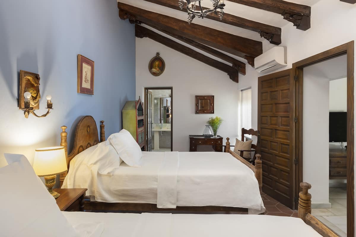 A bedroom with a bed, bedside table, lamp, wall-mounted artwork, and a wooden door.
