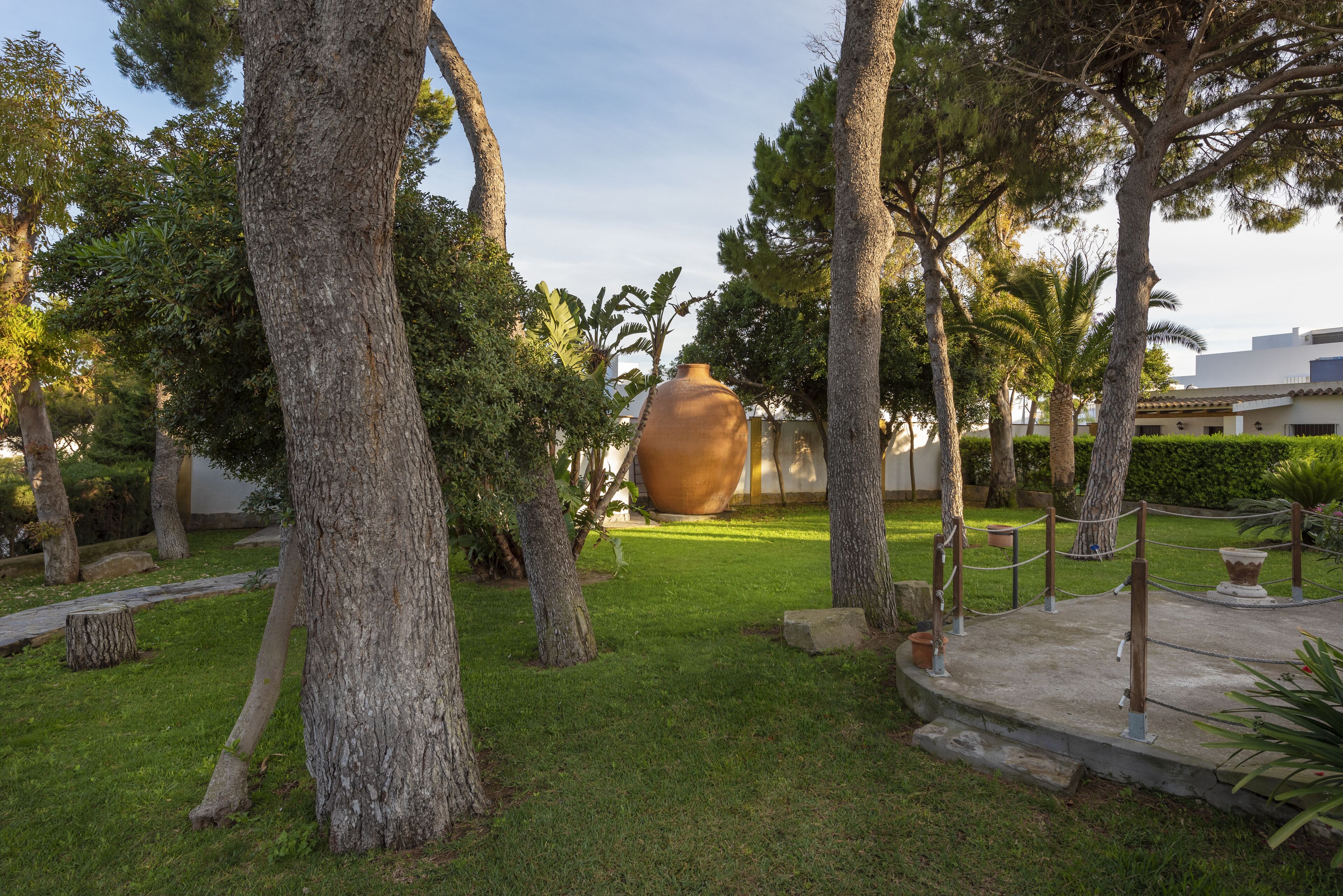 A garden with a large terracotta pot, trees, and a pathway.