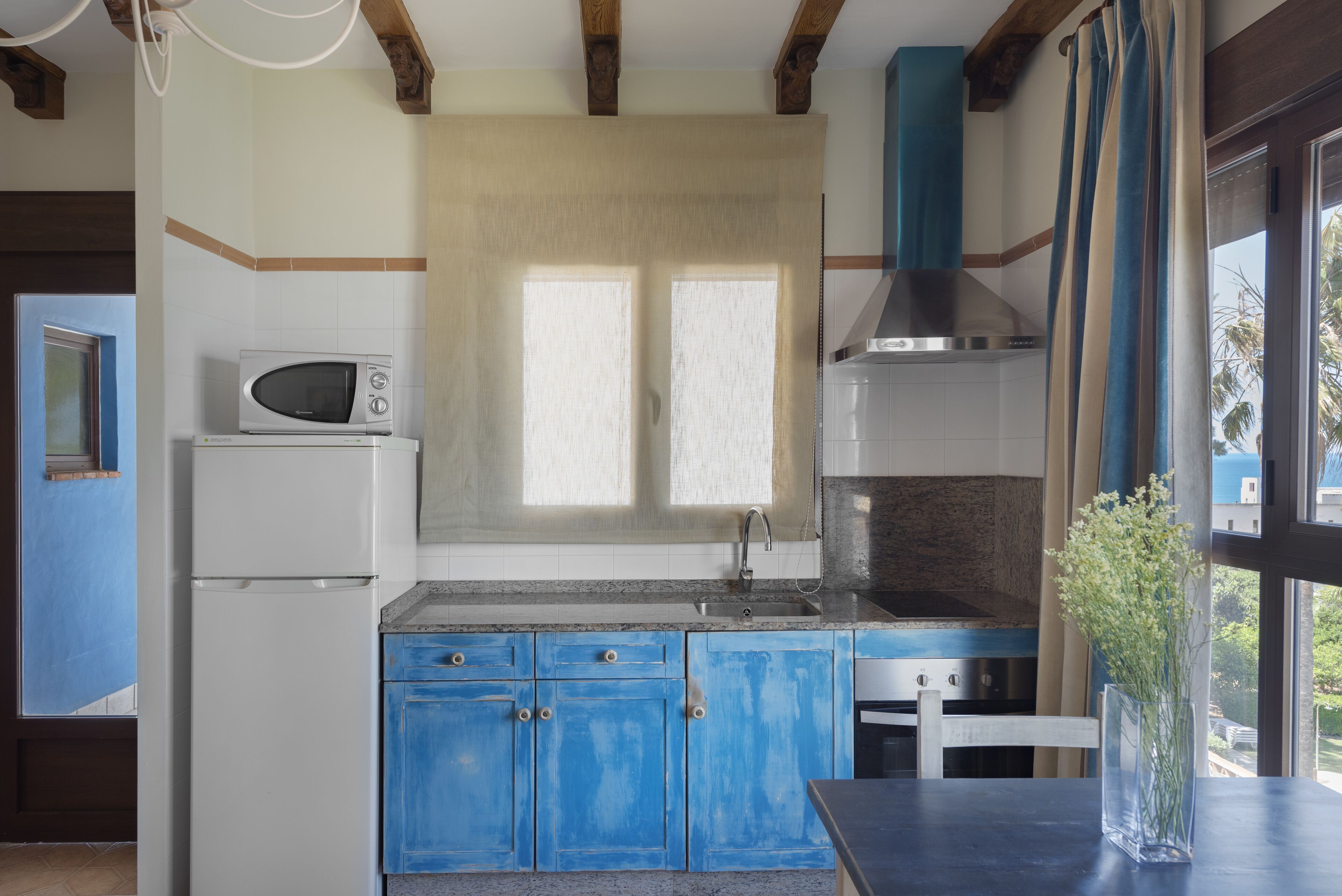 A kitchen with blue cabinets, a white refrigerator, a microwave, and a stove.