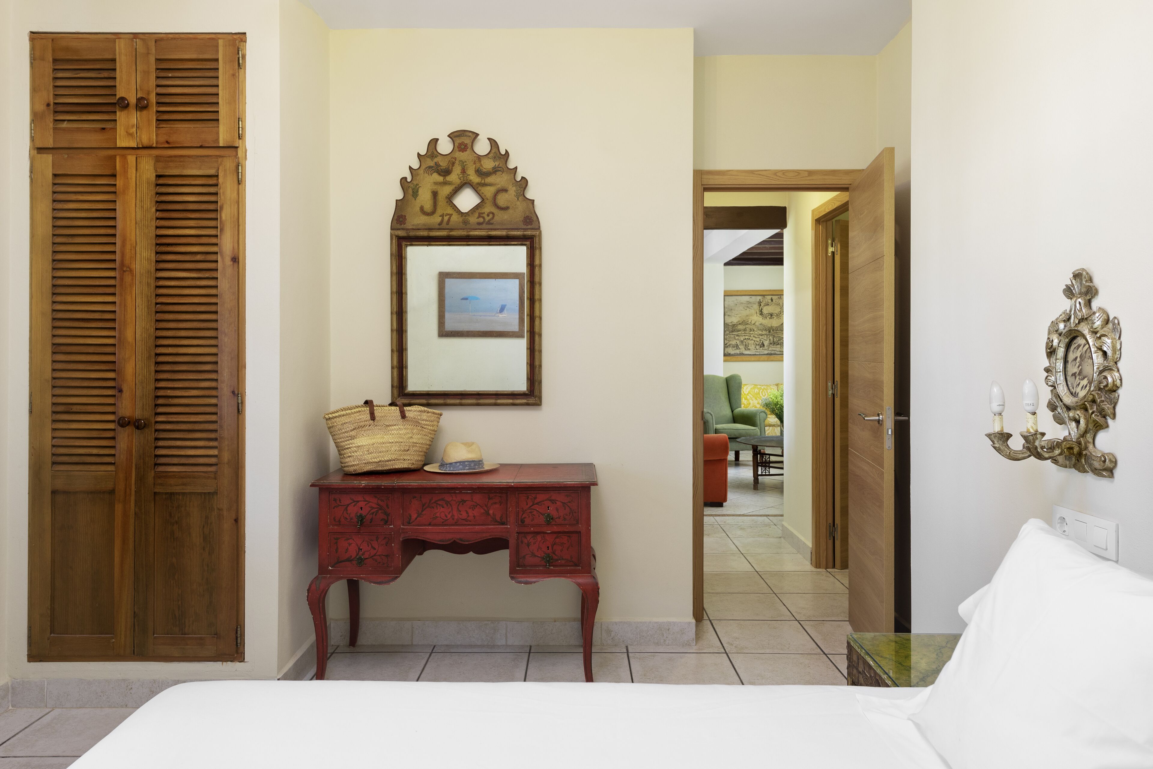 A bedroom with a wooden wardrobe, a red dresser with a mirror, and a bed.
