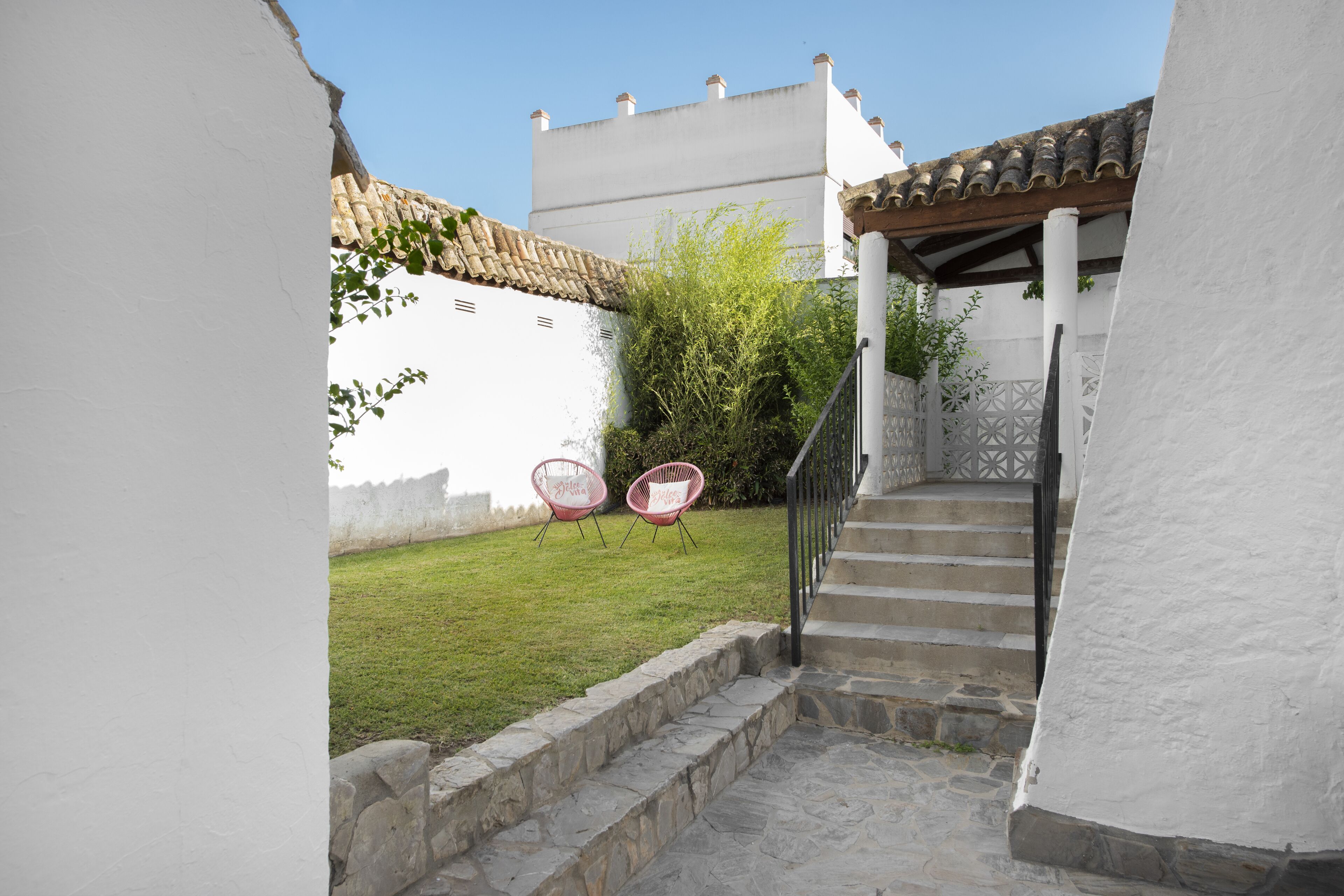 A staircase leading to a covered area with a white wall and a small garden with two pink chairs.