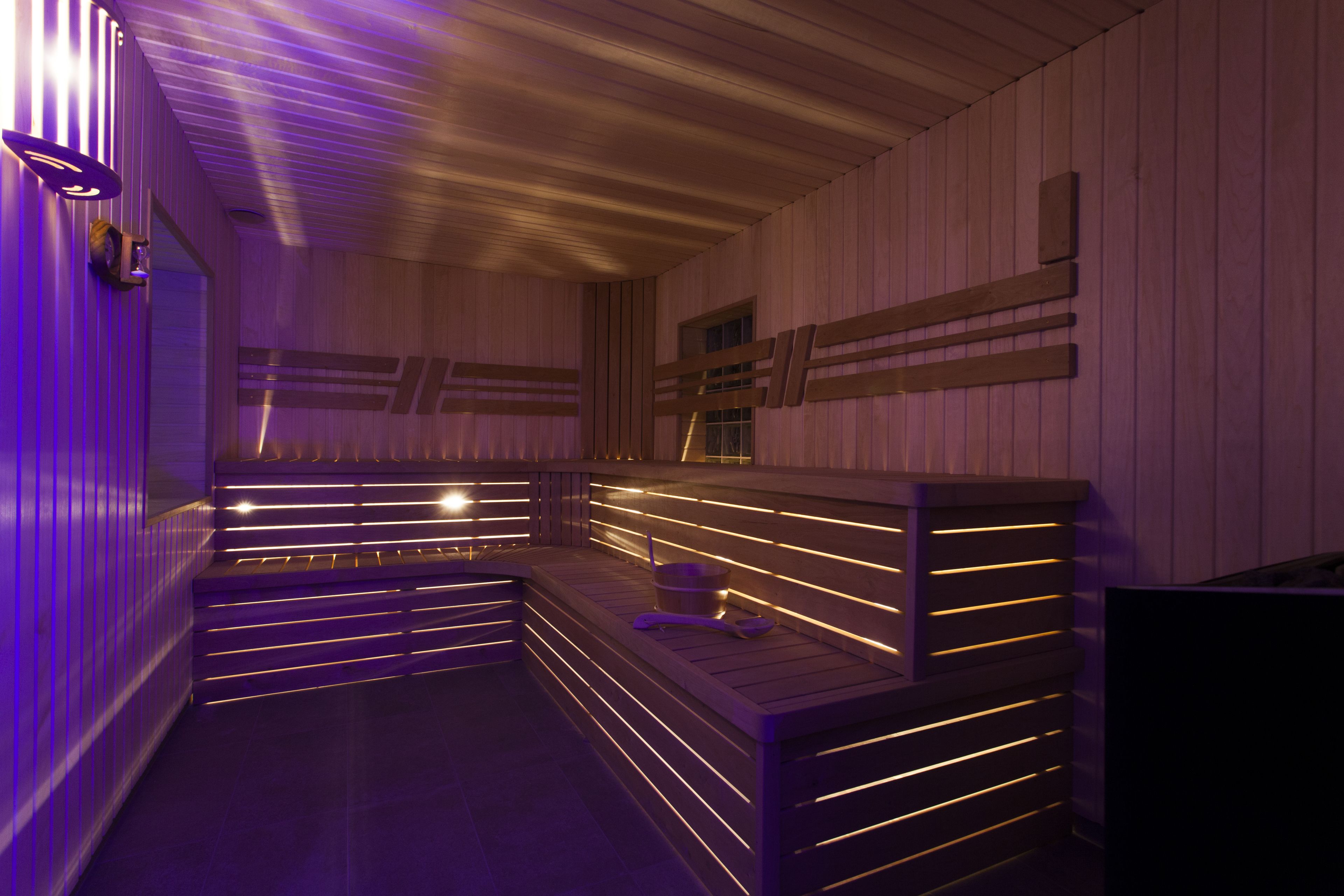 Eine Sauna mit hölzernen Bänken und Lamellenwänden, beleuchtet durch warmes Licht.