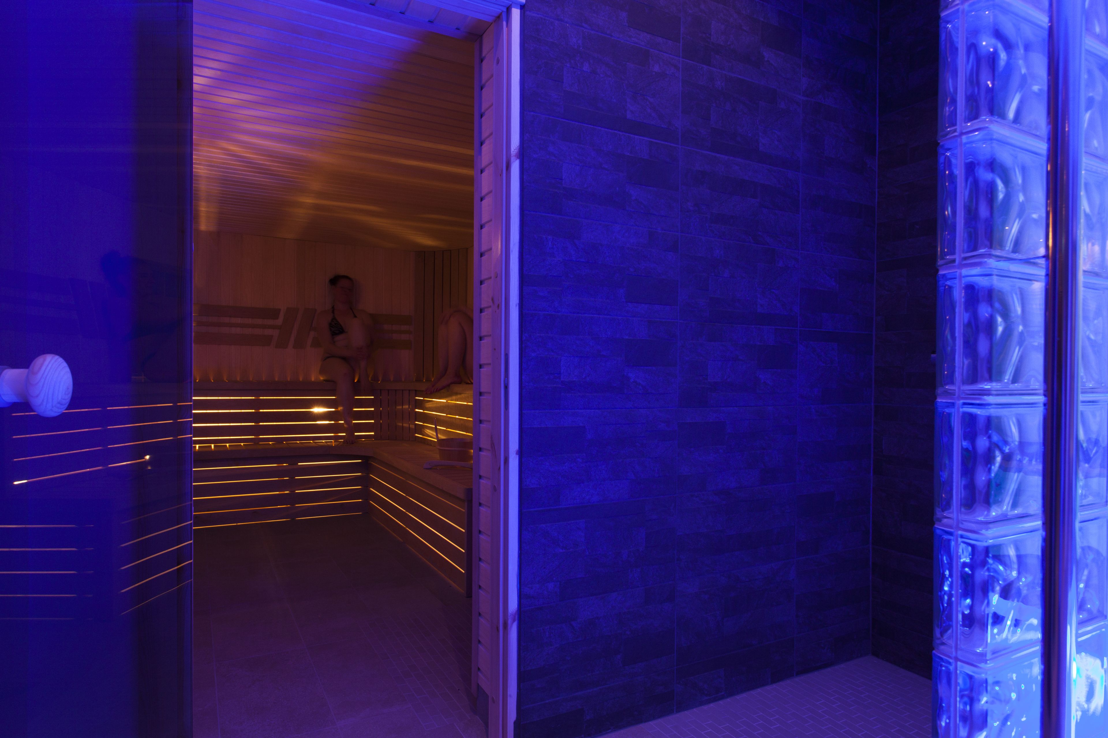 A modern bathroom with a blue-tiled wall, a glass shower enclosure, and a wooden bench.