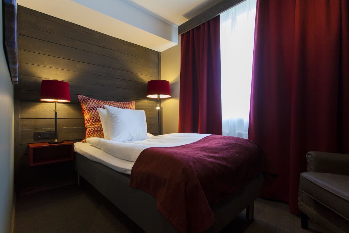 Ein Hotelzimmer mit einem Bett, zwei Nachttischlampen, einem roten Vorhang und einem Sessel.